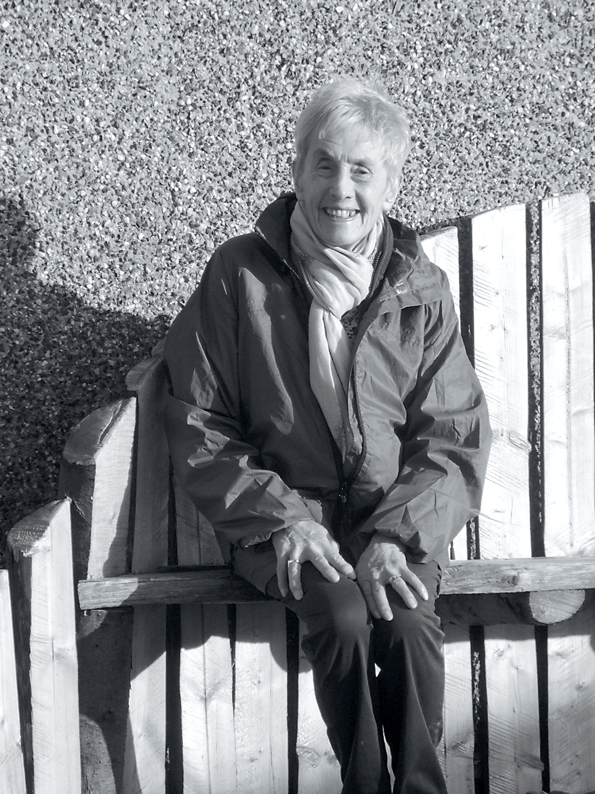 Doris, sits on a hand carved bench made from rough pine logs.