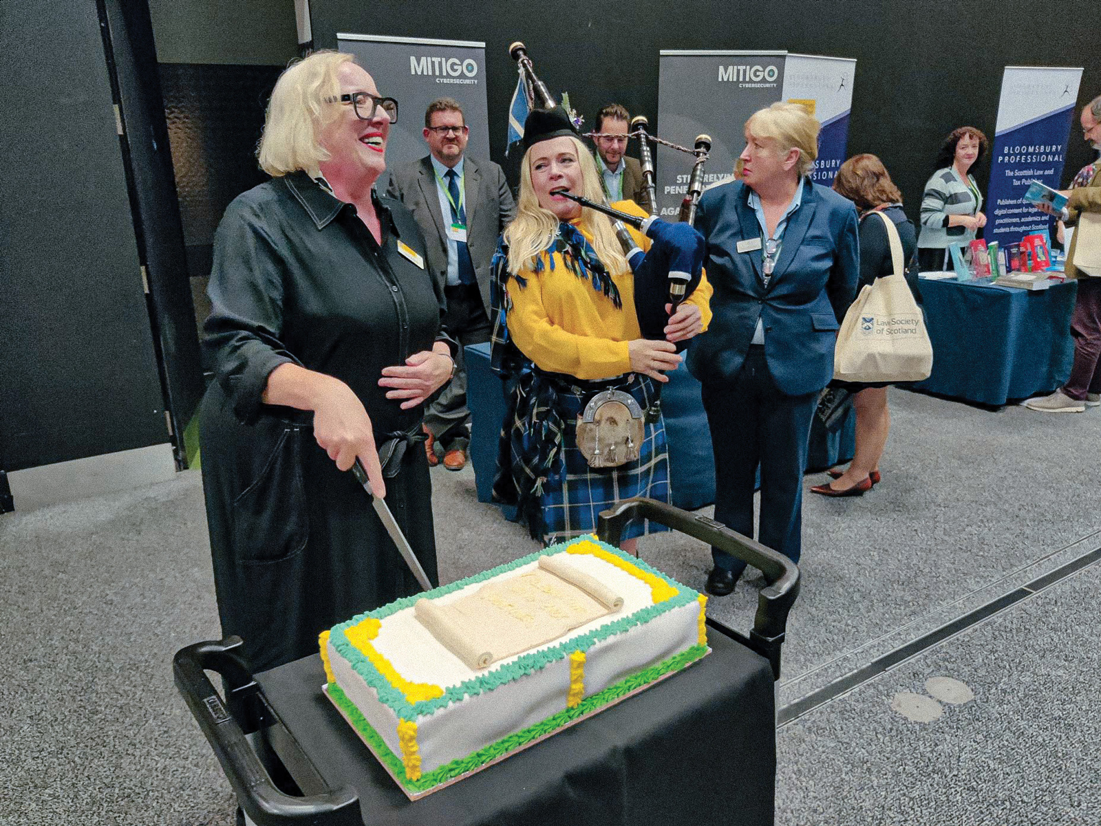 Diane McGiffen cuts the cake celebrating our first in-person conference for three years as a female piper plays