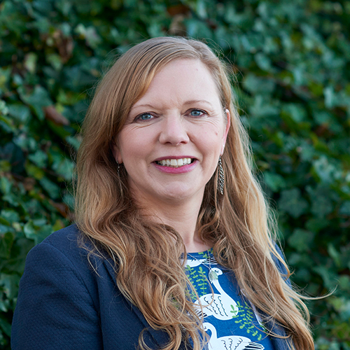 A portrait of Barbara Bolton, in front of a wall of ivy.