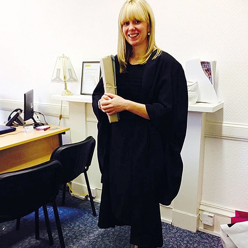 Lindsay Barber, standing by the desk and fireplace in her office, dressed in court robes